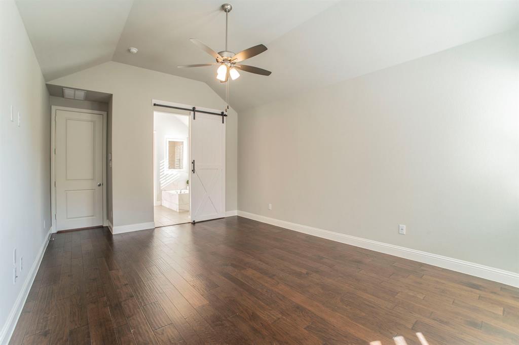 3503 Jersey Road Melissa, TX 75454 - Photo 26 of 40 Unfurnished bedroom featuring a barn door, ceiling fan, vaulted ceiling, dark wood-style floors, and ensuite bathroom