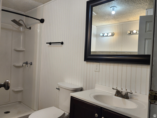 332 Joshua Street Tooele, UT 84074 - Photo 4 of 16 Bathroom featuring white beadboard paneling, a dark wood-finish vanity with an integrated sink, a framed mirror, and a shower stall with a rain showerhead