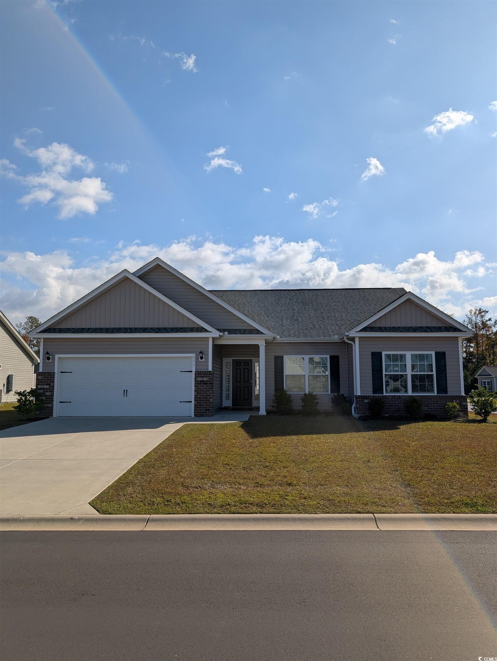 View of front of home featuring a front lawn, driveway, brick siding, board and batten siding, and a shingled roof