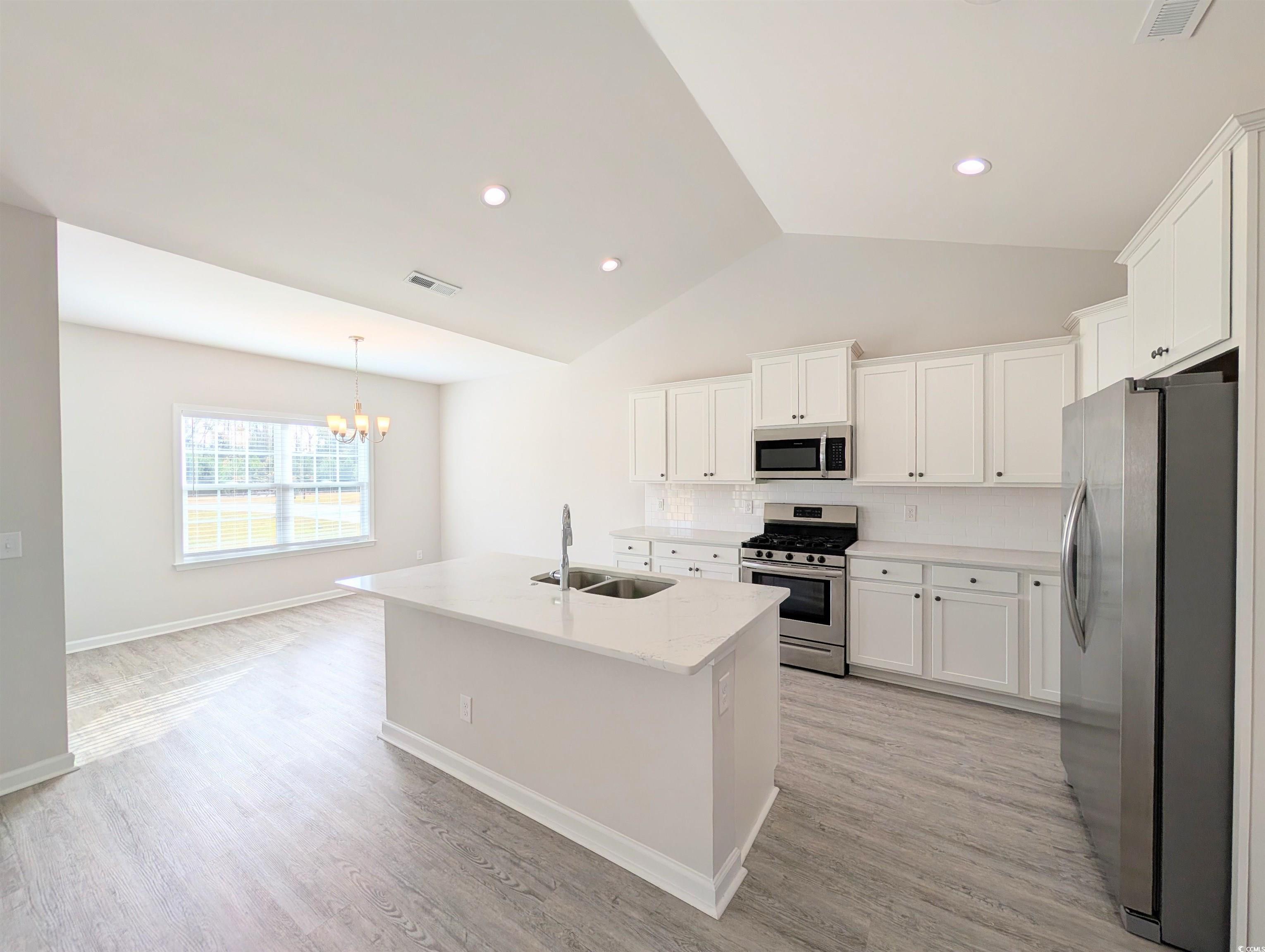 351 Lakota Loop Longs, SC 29568 - Photo 5 of 31 Kitchen featuring stainless steel appliances, a center island with sink, white cabinets, light wood-style flooring, and vaulted ceiling