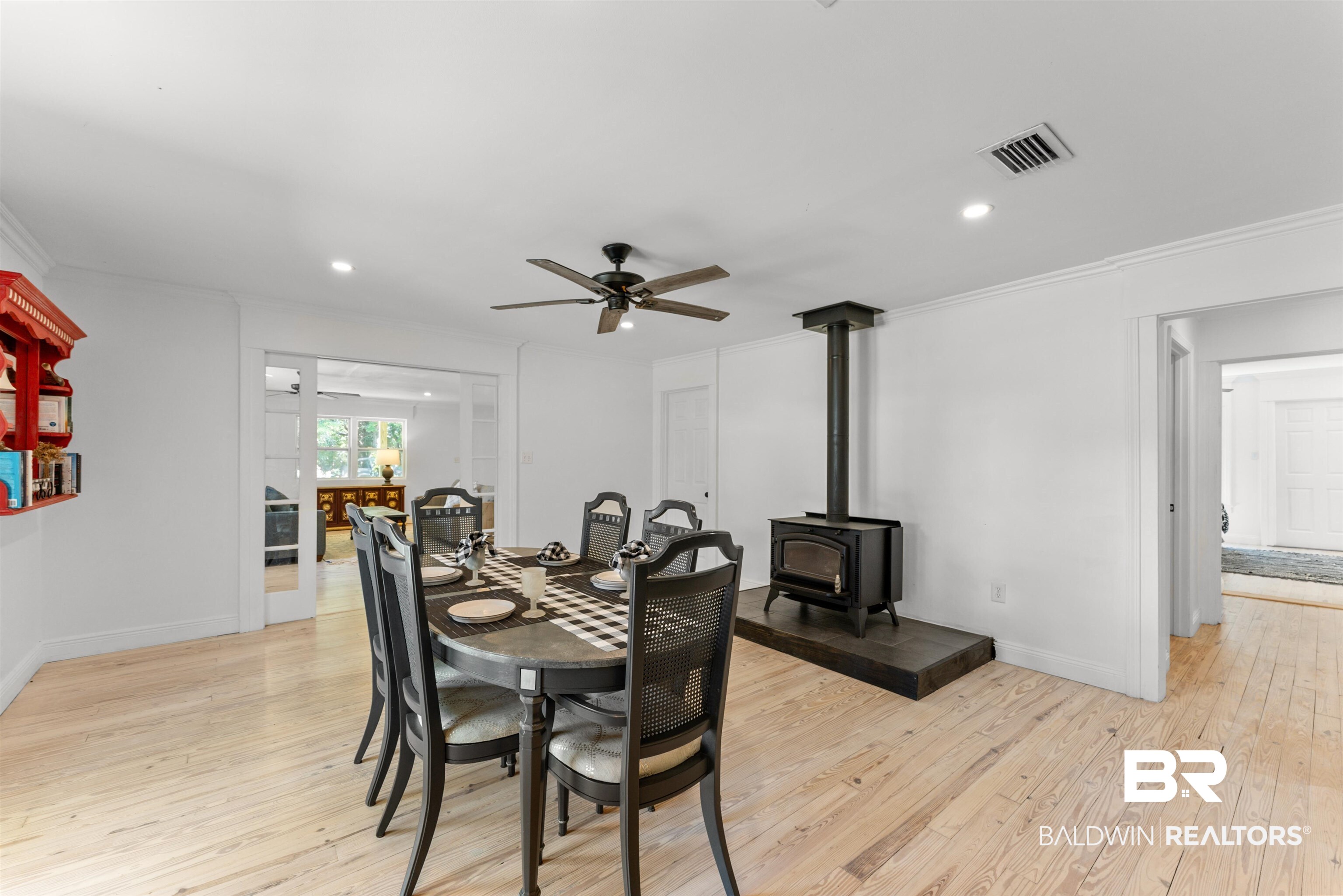 6447 Bemis Lane Bon Secour, AL 36511 - Photo 25 of 62 Dining area featuring a black wood-burning stove on a dark-toned hearth, wood-finish flooring, and a ceiling fan with integrated lighting