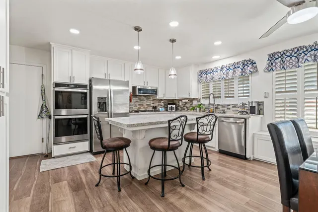 a kitchen with stainless steel appliances kitchen island granite countertop a refrigerator a stove a sink and chairs with wooden floor