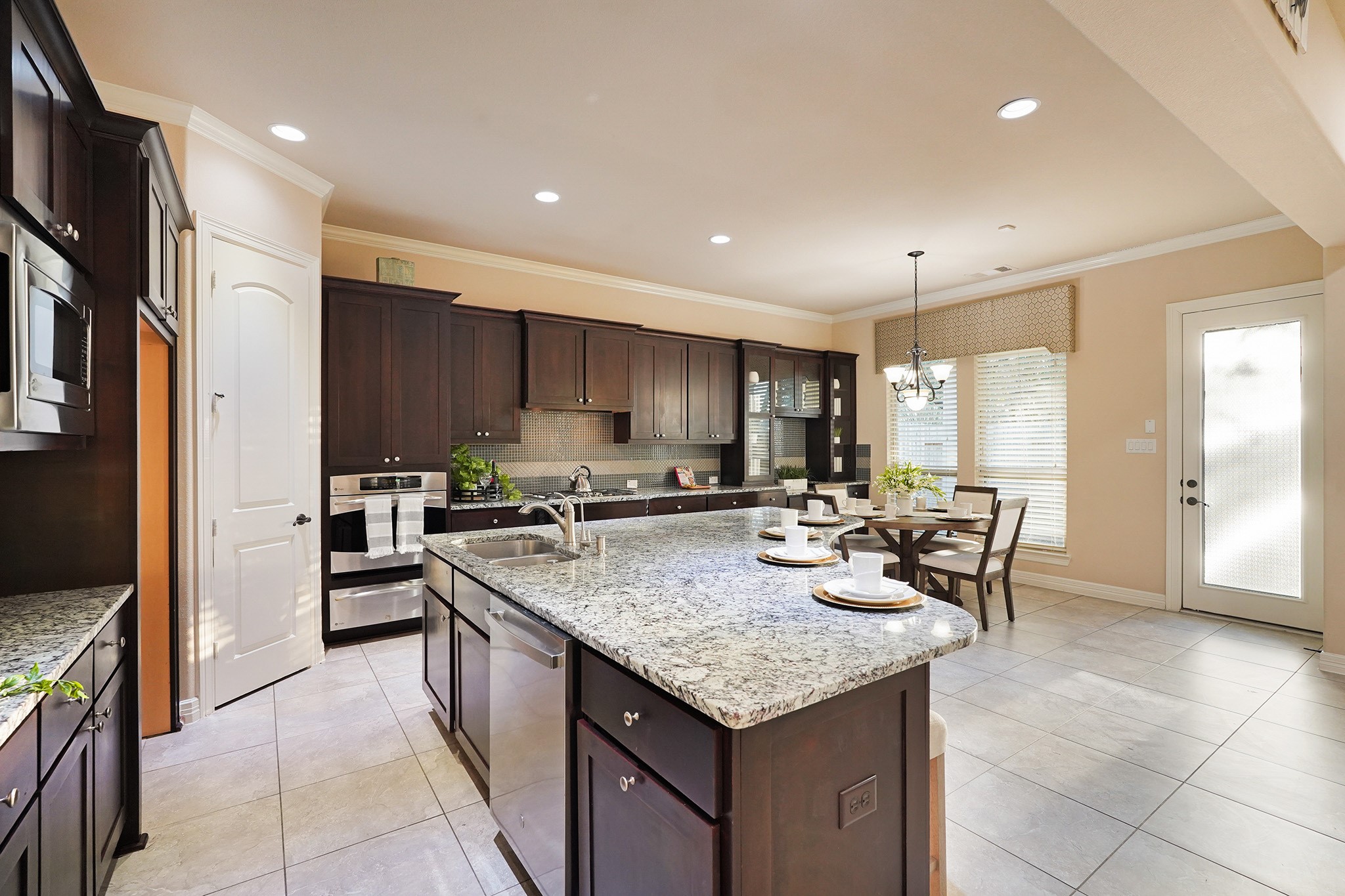 3102 Barrons Way Sugar Land, TX 77479 - Photo 14 of 42 This spacious kitchen features dark wood cabinetry, a large granite island with seating, stainless steel appliances, and a bright dining area with natural light from large windows and a glass door.
