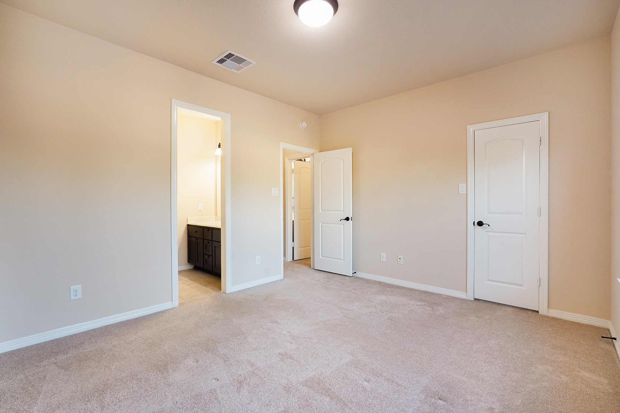 3102 Barrons Way Sugar Land, TX 77479 - Photo 27 of 42 SECOND Flr-Bed#4: This photo shows a bright, spacious bedroom with neutral walls and carpet. It features a ceiling light, white trim, and two doors, one leading to a bathroom with dark cabinetry.