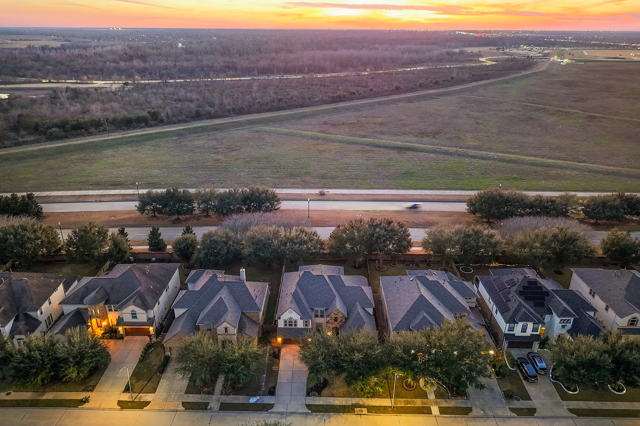 3102 Barrons Way Sugar Land, TX 77479 - Photo 37 of 42 This aerial photo showcases a row of suburban homes with well-maintained lawns and driveways, set against the backdrop of a spacious open field, offering a serene and spacious environment. The sunset in the distance adds a warm, inviting glow to the neighborhood.