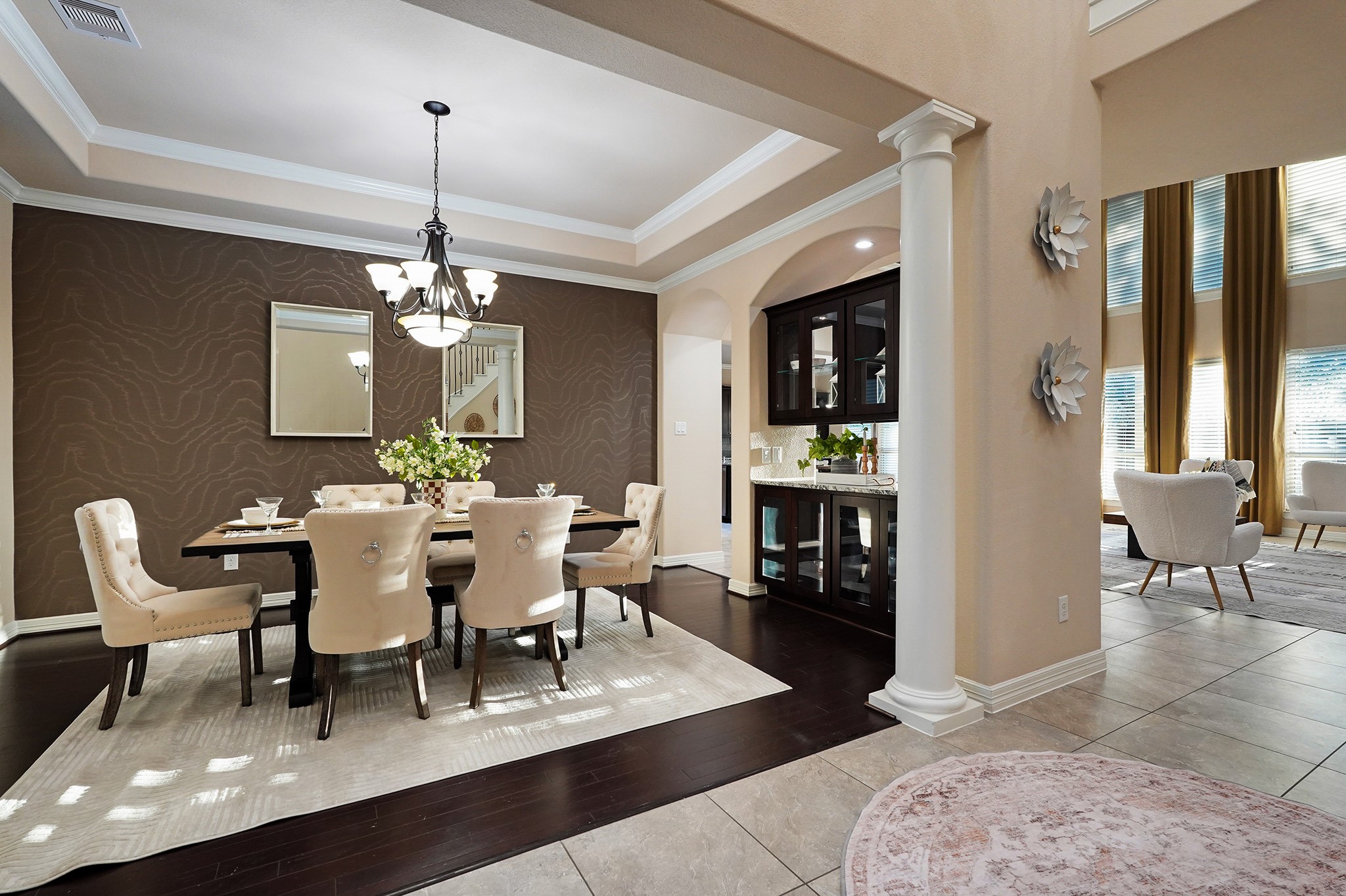 3102 Barrons Way Sugar Land, TX 77479 - Photo 4 of 42 This elegant dining area features a stylish chandelier, coffered ceiling, and a warm accent wall. It opens to a bright living space with tall windows and high ceilings, offering a sophisticated and inviting atmosphere.