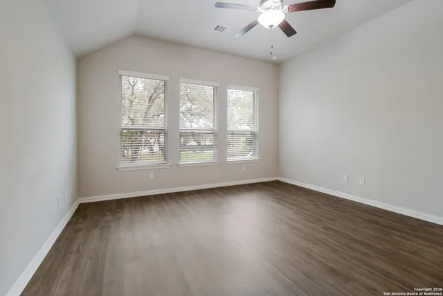 an empty room with wooden floor chandelier fan and windows