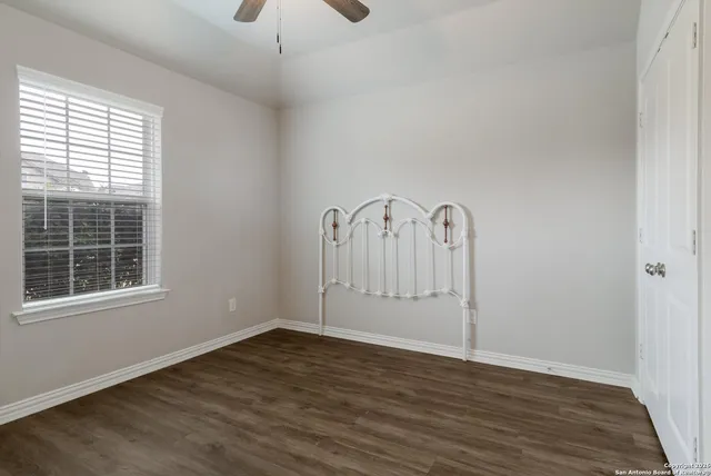 an empty room with wooden floor a ceiling fan and windows