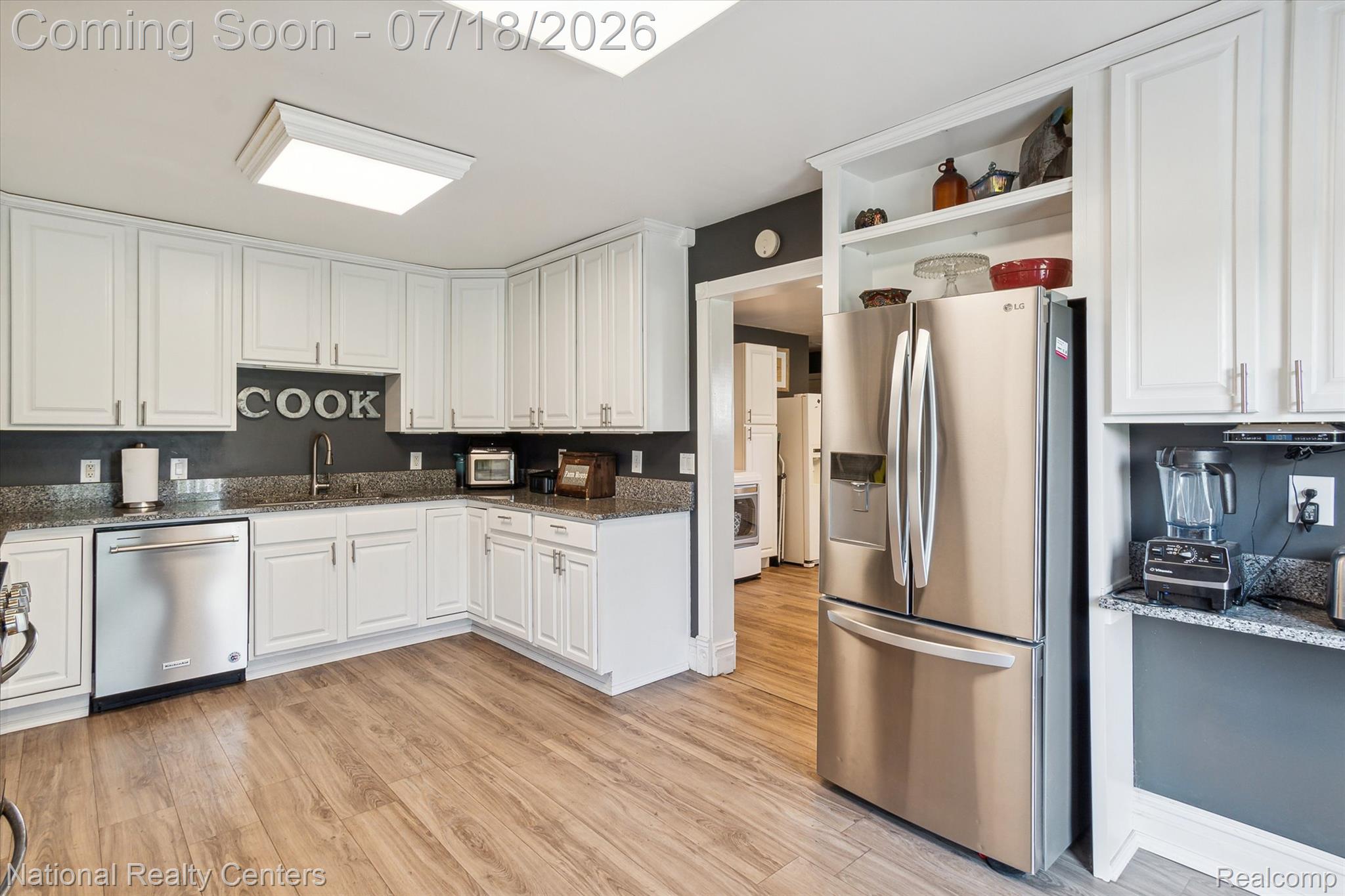 9589 Clinton Macon Road Tecumseh, MI 49286 - Photo 19 of 48 Kitchen featuring wood-finish flooring, white cabinetry, a stainless steel dishwasher, a stainless steel refrigerator, and granite countertops