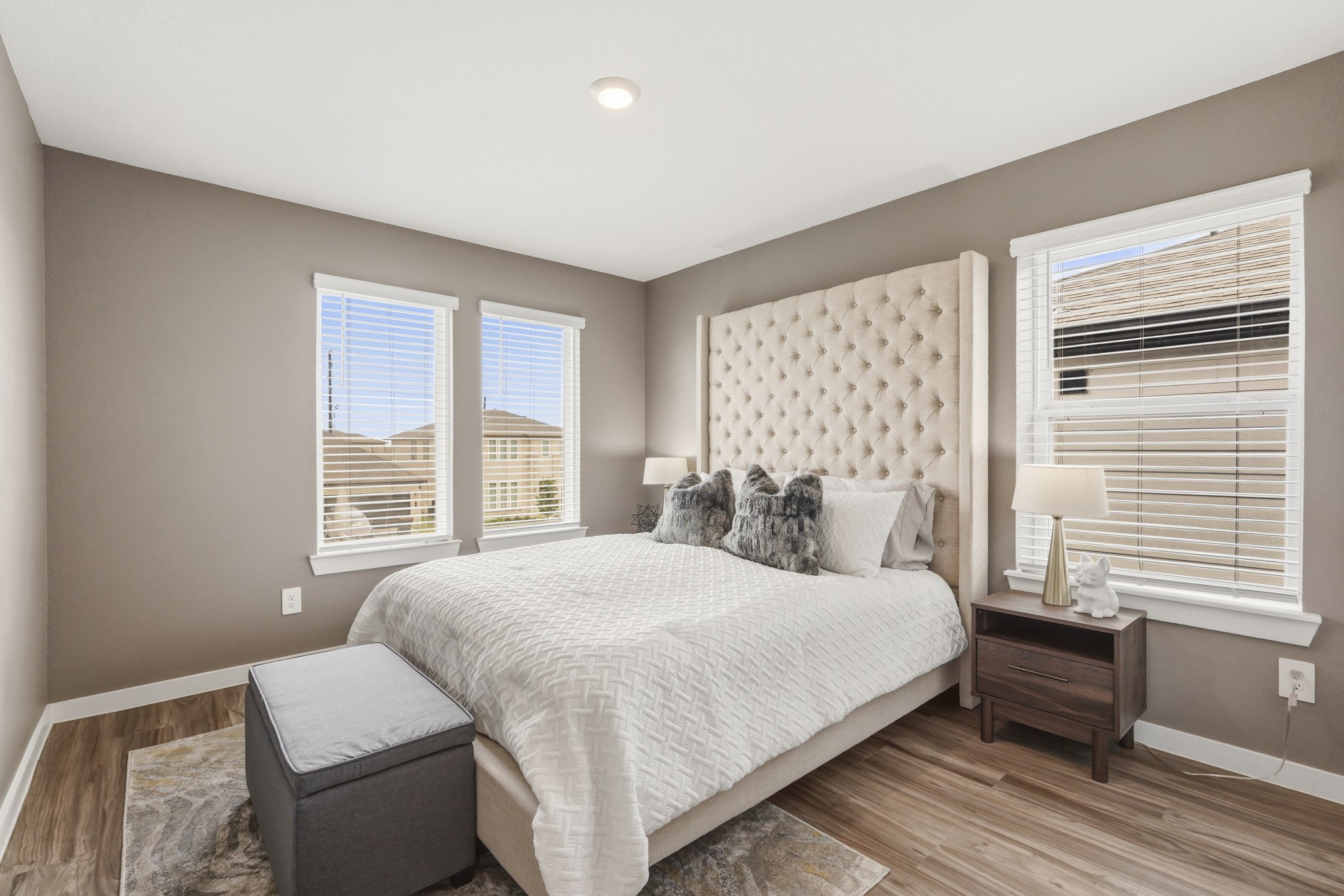 22522 Modica Rift Lane Katy, TX 77449 - Photo 29 of 38 Warm, welcoming, and beautifully appointed, this secondary bedroom feels like a true guest suite. Soft taupe walls, a wall of windows flooding the space with natural light, and a dramatically tall tufted upholstered headboard create a room that feels effortlessly elevated. Cozy layered bedding, warm wood nightstands, and a sleek storage ottoman at the foot of the bed make this a space any guest would feel honored to call their own.