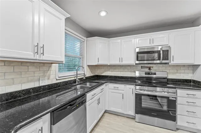 a kitchen with granite countertop a sink dishwasher stove and microwave with wooden cabinets