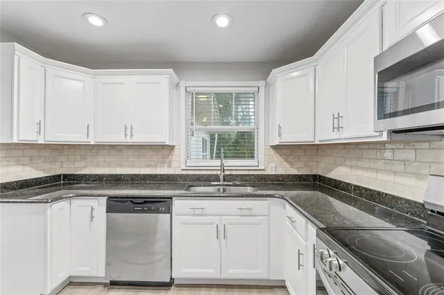 a kitchen with granite countertop white cabinets stainless steel appliances a sink and a window