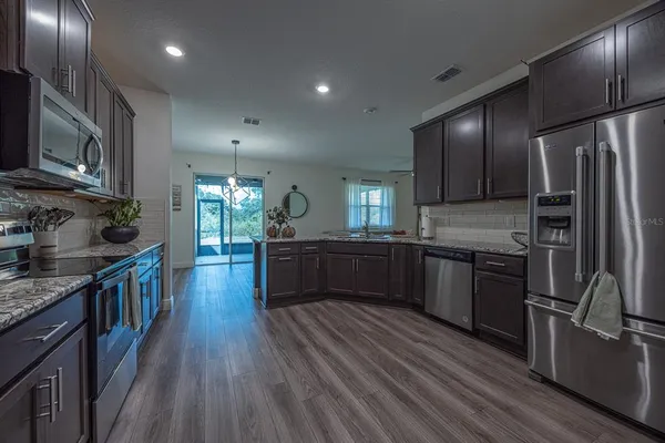 a kitchen with stainless steel appliances granite countertop a refrigerator a stove top oven a sink dishwasher and wooden cabinets with wooden floor