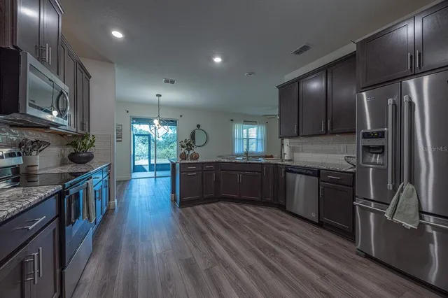 a kitchen with stainless steel appliances granite countertop a refrigerator a stove top oven a sink dishwasher and wooden cabinets with wooden floor
