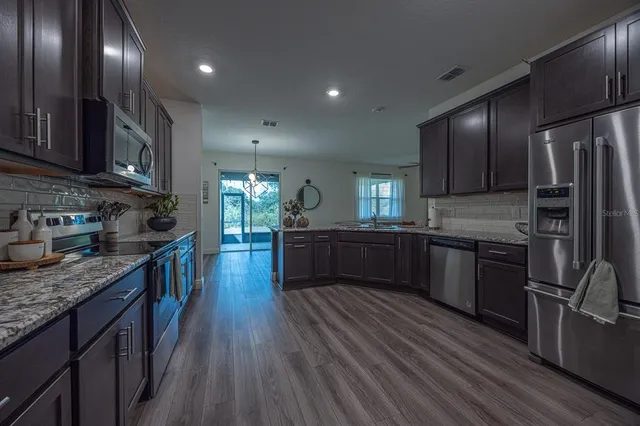 a kitchen with stainless steel appliances granite countertop wooden cabinets a refrigerator a sink a stove and a wooden floors