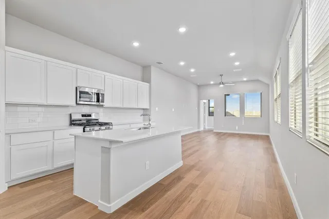 a kitchen with stainless steel appliances granite countertop a stove a sink and white cabinets with wooden floor