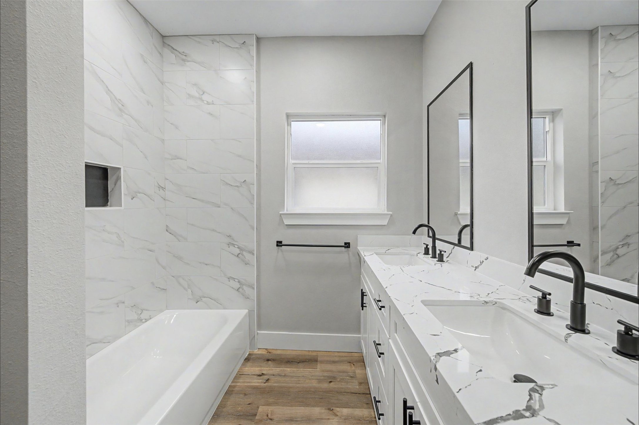 2338 Lidstone Street Houston, TX 77023 - Photo 14 of 17 Bathroom with a double vanity, quartz countertops, and plenty cabinet space. It includes a full size bathtub with a built-in niche and a large mirror, complemented by stylish black fixtures. A frosted window provides natural light and privacy.