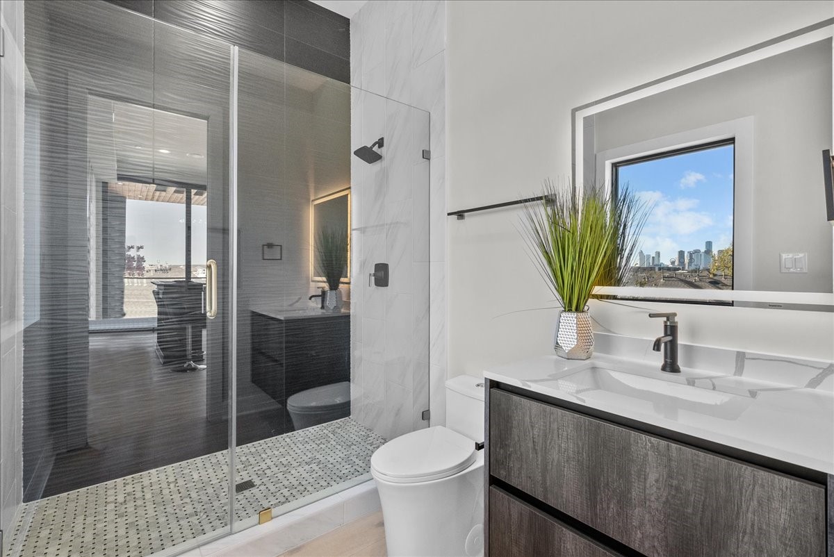 516 Reinerman Street Houston, TX 77007 - Photo 27 of 42 This modern bathroom features a sleek design with a glass-enclosed shower, stylish vanity, and large mirror. A window offers natural light and urban views, enhancing the space's contemporary feel.