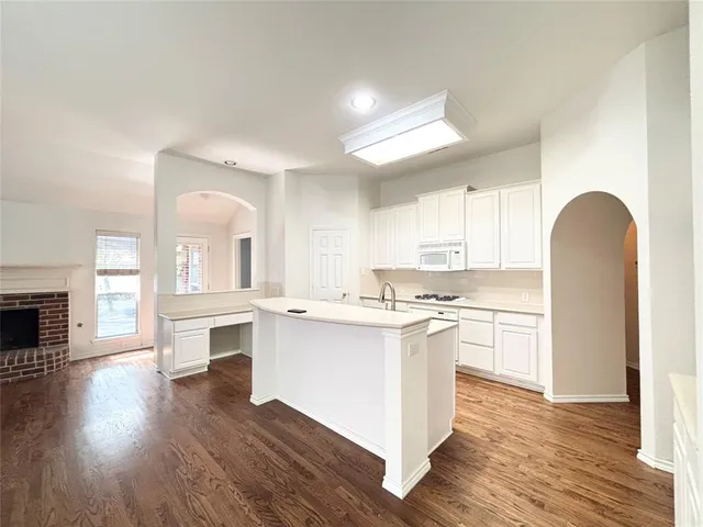 a kitchen with stainless steel appliances a stove top oven a sink a refrigerator and white cabinets with wooden floor