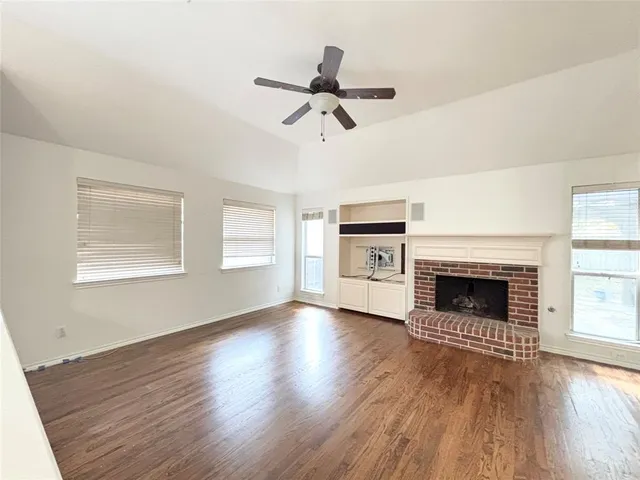 an empty room with wooden floor fireplace and windows
