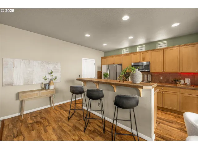 a kitchen with stainless steel appliances kitchen island granite countertop a refrigerator a stove a dining table and chairs with wooden floor