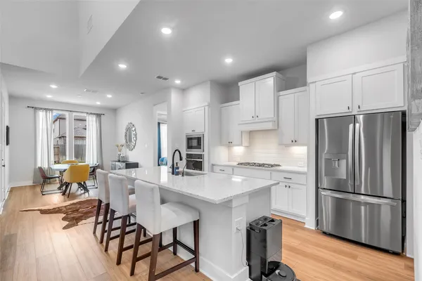a kitchen with stainless steel appliances a refrigerator a stove a sink a dining table and chairs with wooden floor