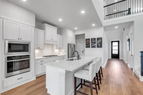 a kitchen with stainless steel appliances granite countertop a stove a sink a microwave a refrigerator white cabinets and wooden floor