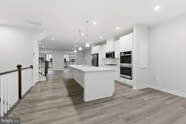 a large white kitchen with kitchen island a sink wooden floor and stainless steel appliances