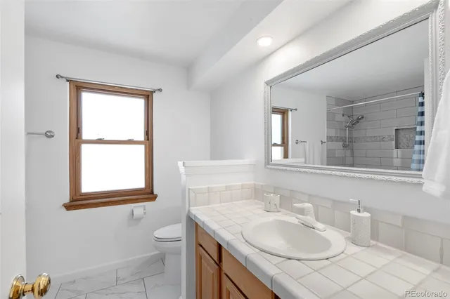 a bathroom with a granite countertop sink toilet a mirror and a window