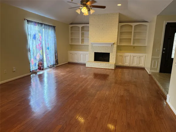 an empty room with wooden floor fireplace and windows