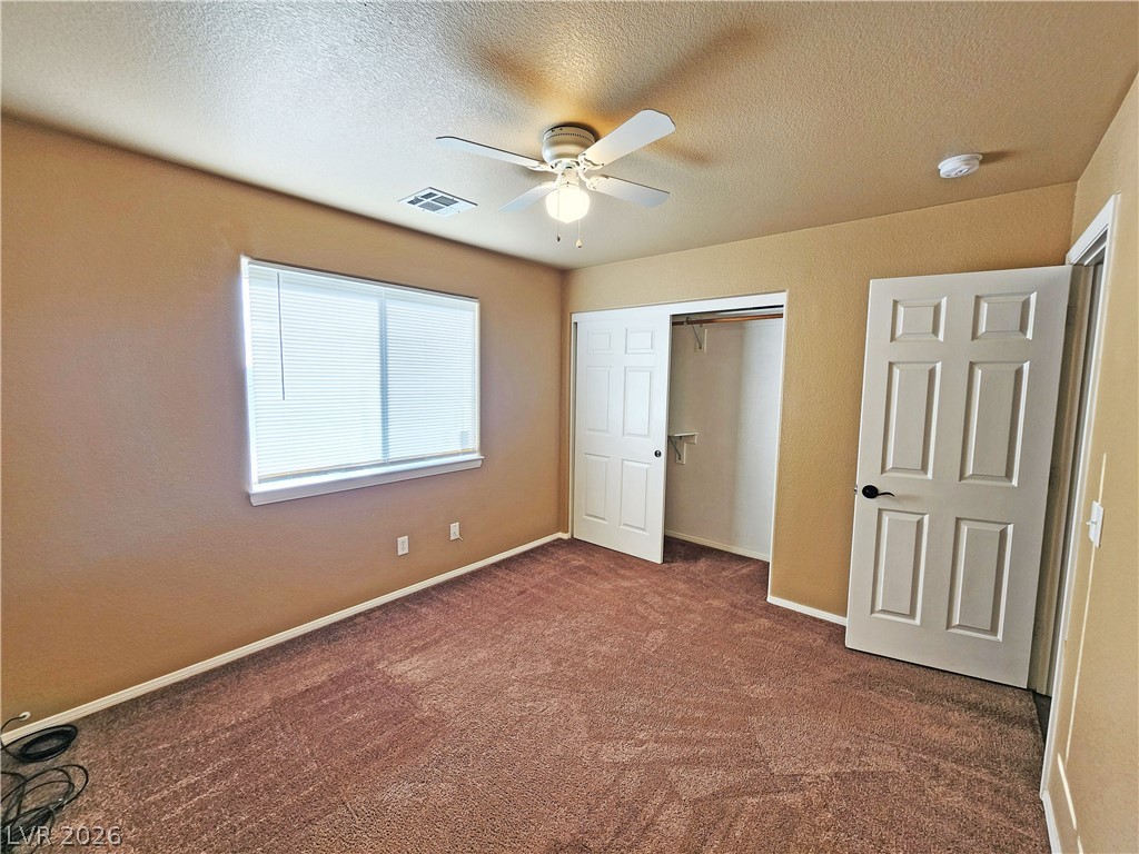 3680 Ravine Avenue Pahrump, NV 89048 - Photo 24 of 28 Unfurnished bedroom featuring dark colored carpet, a textured ceiling, visible vents, a closet, and ceiling fan