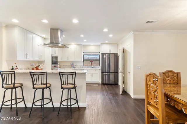 a kitchen with stainless steel appliances kitchen island granite countertop a table chairs refrigerator and microwave