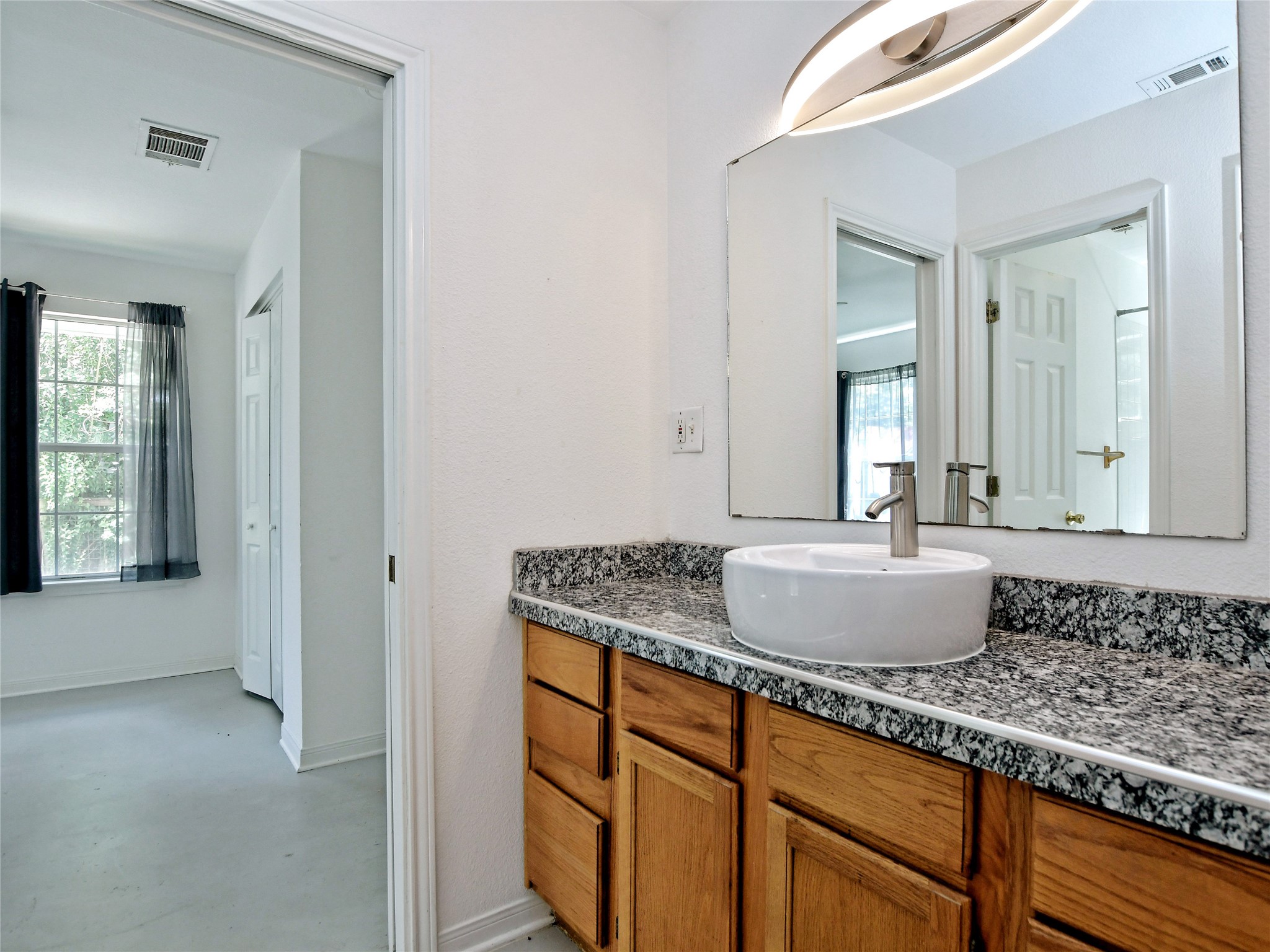 4604 Red River Street, Unit A Austin, TX 78751 - Photo 9 of 15 Vanity featuring a vessel sink with a brushed metal faucet, granite-patterned countertop, and wood-finish cabinetry
