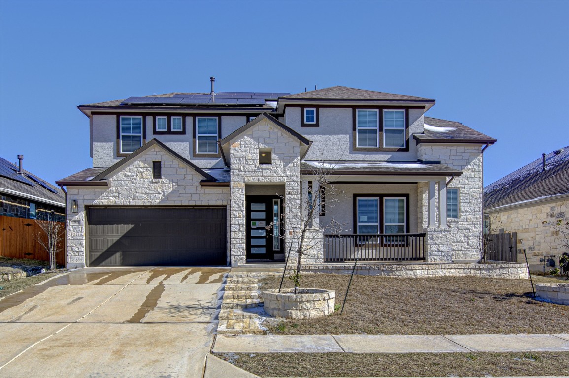 French country inspired facade with a porch, driveway, solar panels, stone siding, and stucco siding