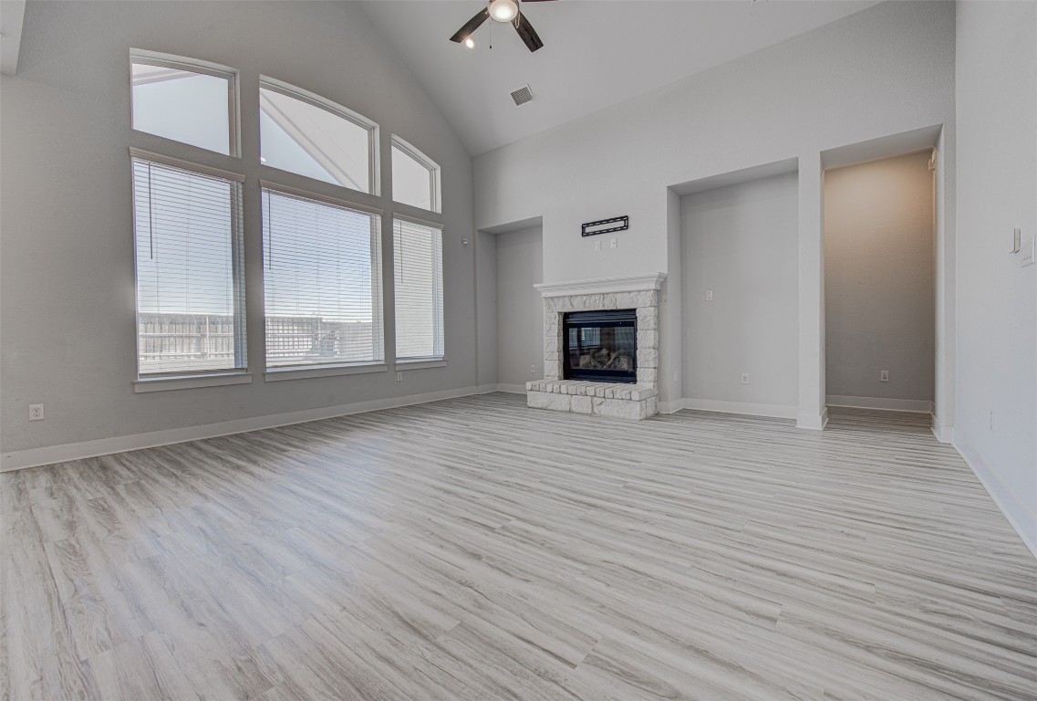 822 Wild Pecan Loop Buda, TX 78610 - Photo 13 of 33 Unfurnished living room featuring high vaulted ceiling, a stone fireplace, light wood-style floors, and a ceiling fan