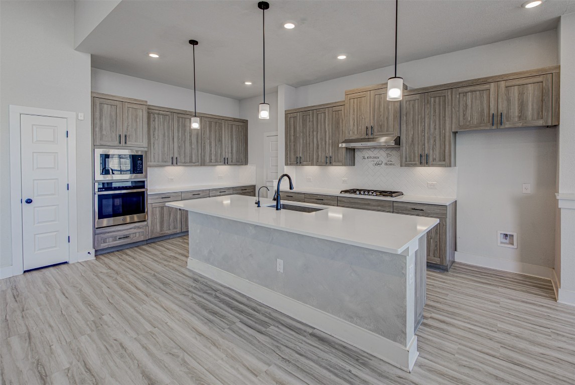 822 Wild Pecan Loop Buda, TX 78610 - Photo 5 of 33 Kitchen with hanging light fixtures, stainless steel appliances, an island with sink, light wood-style flooring, and recessed lighting