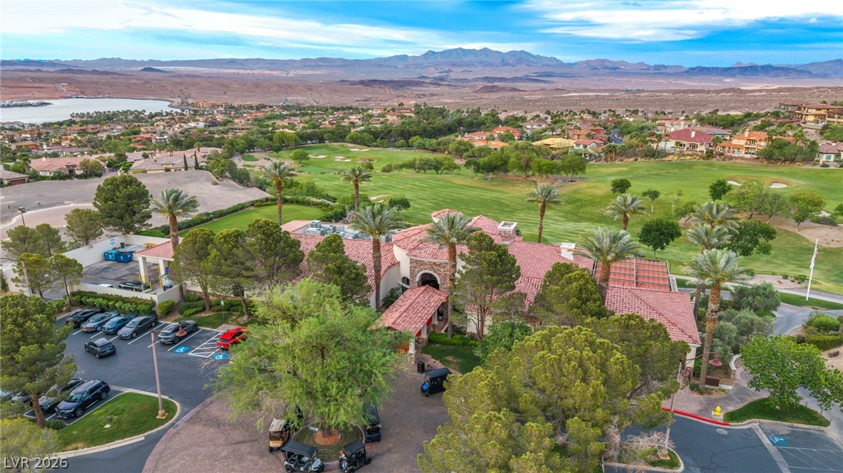 3 Rue Promenade Way Henderson, NV 89011 - Photo 23 of 26 An aerial panorama reveals a golf course, parking area, and a building under red-tiled roofs, framed by distant mountains and a serene lake.