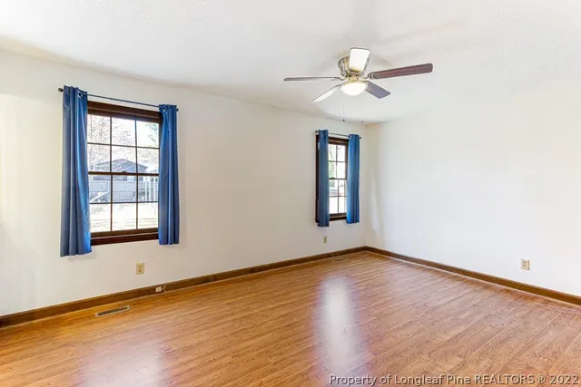an empty room with wooden floor chandelier fan and windows