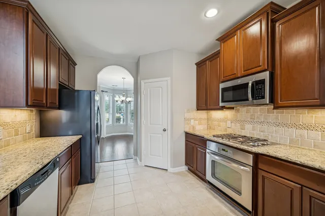 a view of an empty room with wooden floor a ceiling fan and a kitchen view