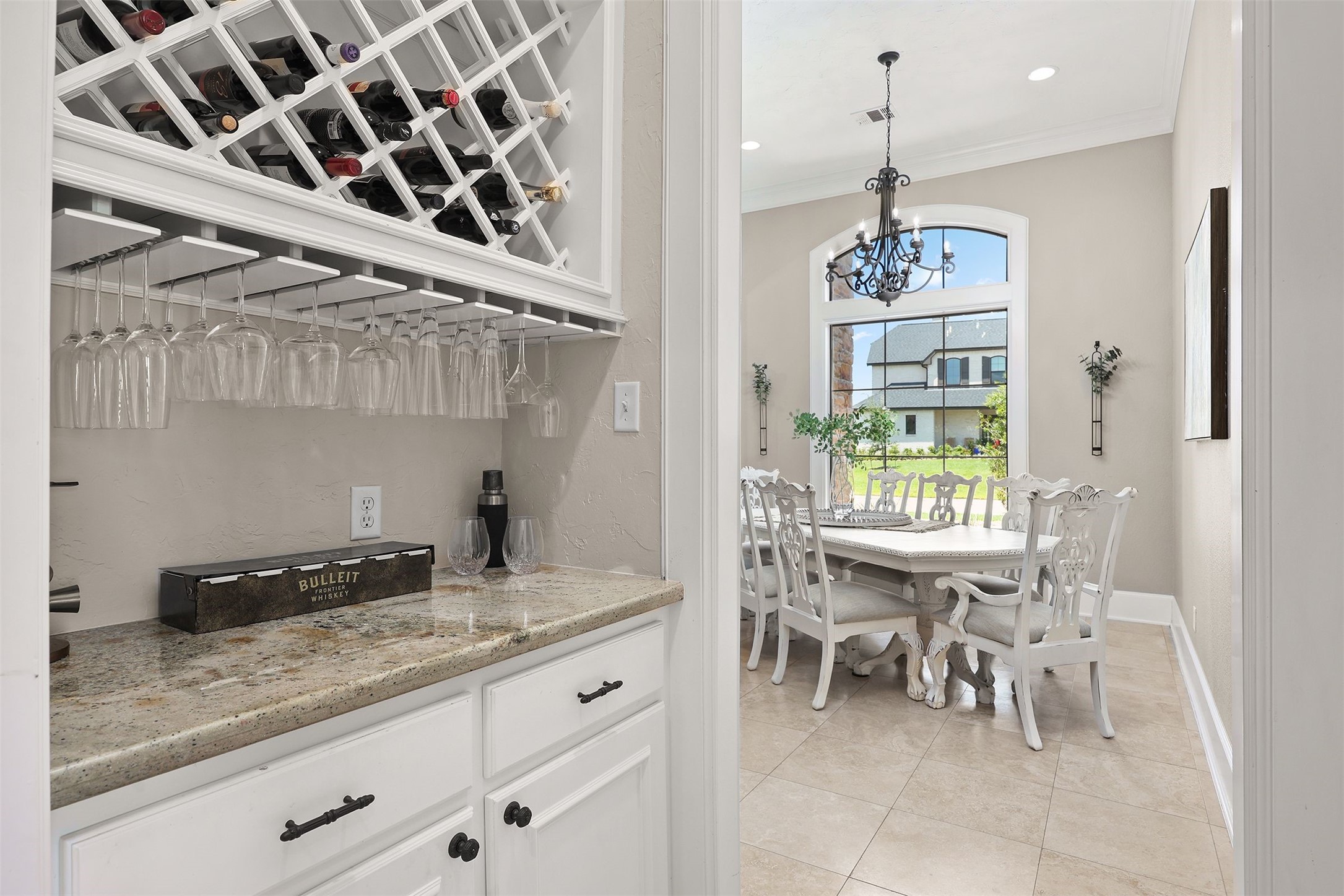 10896 Decatur Street Willis, TX 77318 - Photo 18 of 50 This inviting dining area features elegant white furniture, abundant natural light from a large window, a chic chandelier, and an adjacent cozy bar nook with wine storage and glass racks, perfect for entertaining.