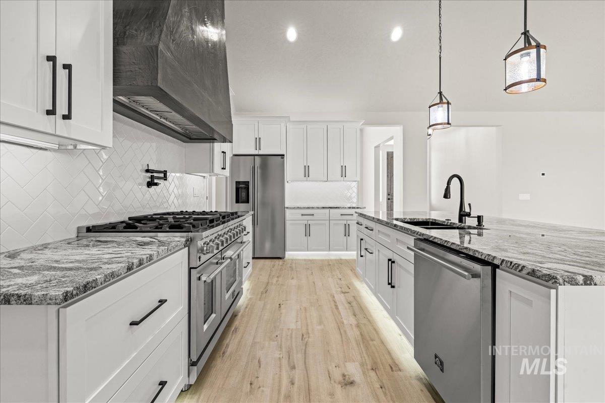 23735 Legends Lane Caldwell, ID 83607 - Photo 14 of 34 Kitchen featuring stainless steel appliances, decorative backsplash, custom range hood, light stone counters, and light wood-style floors