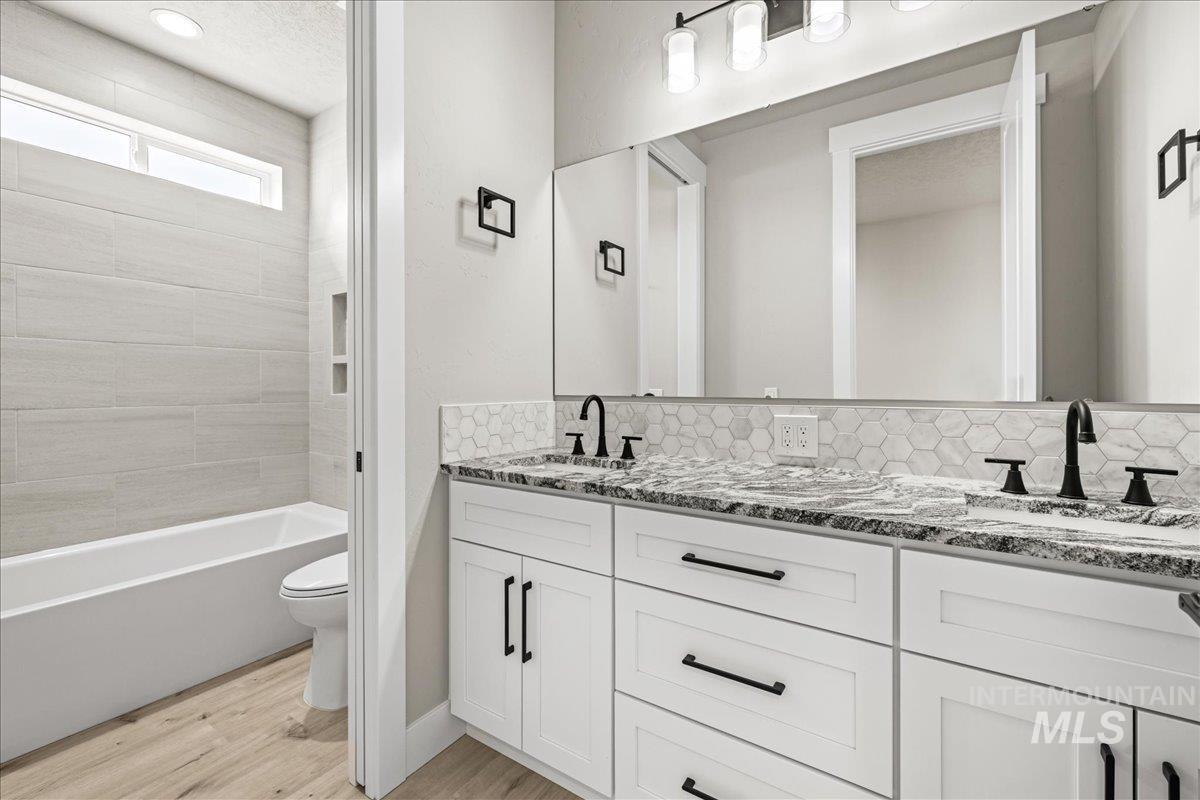 23735 Legends Lane Caldwell, ID 83607 - Photo 25 of 34 Full bath featuring light wood-style flooring, double vanity, tasteful backsplash, bathing tub / shower combination, and a textured ceiling