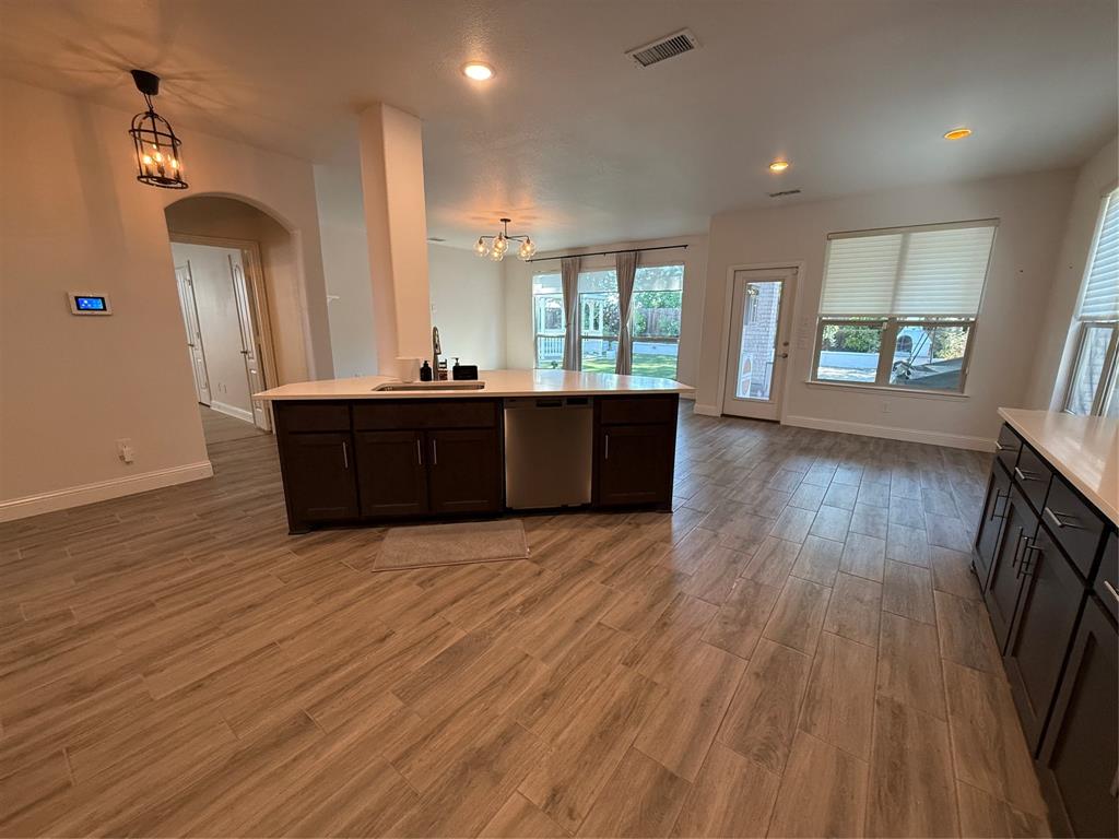 5212 Troupe Road McKinney, TX 75071 - Photo 8 of 38 Open-concept kitchen and living area featuring wood-finish tile flooring, a kitchen island with dark cabinetry and light countertops, recessed lighting, and a glass-paneled exterior door
