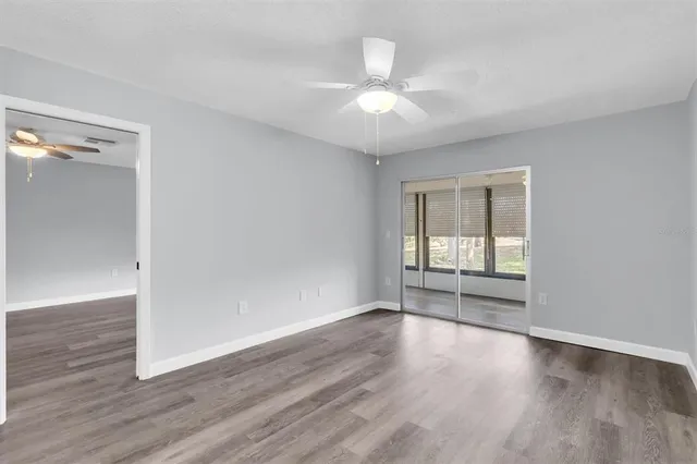 an empty room with wooden floor fan and windows