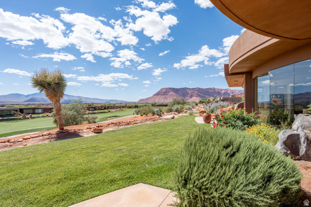 2331 West Entrada Trail, Unit 61 St. George, UT 84770 - Photo 56 of 69 Expansive outdoor living area featuring a verdant lawn, mature desert landscaping, and a curved stucco exterior with large windows