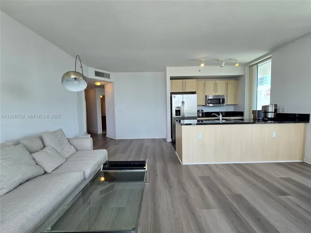 a living room with stainless steel appliances furniture a rug and a kitchen view