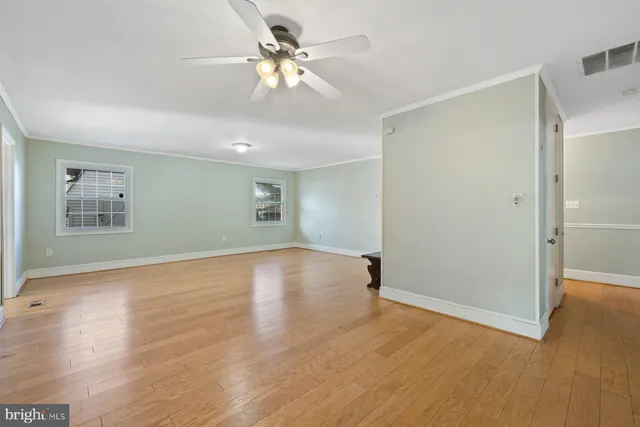 an empty room with wooden floor chandelier fan and windows