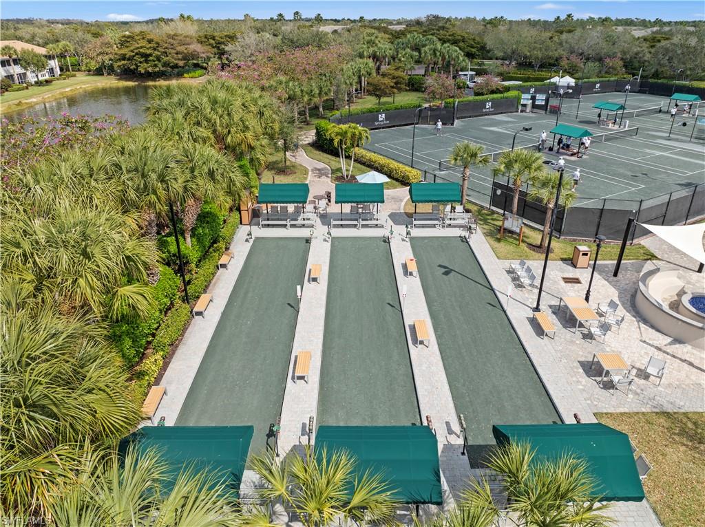 9331 Spring Run Boulevard, Unit 3005 Estero, FL 34135 - Photo 44 of 48 Multiple bocce ball courts with shaded seating, tennis courts with a dark perimeter fence, a fire pit area, and a tranquil pond bordered by lush tropical landscaping