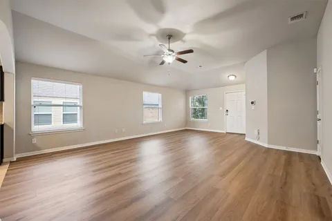 an empty room with wooden floor ceiling fan and windows