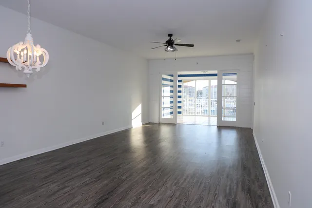 an empty room with wooden floor chandelier fan and windows